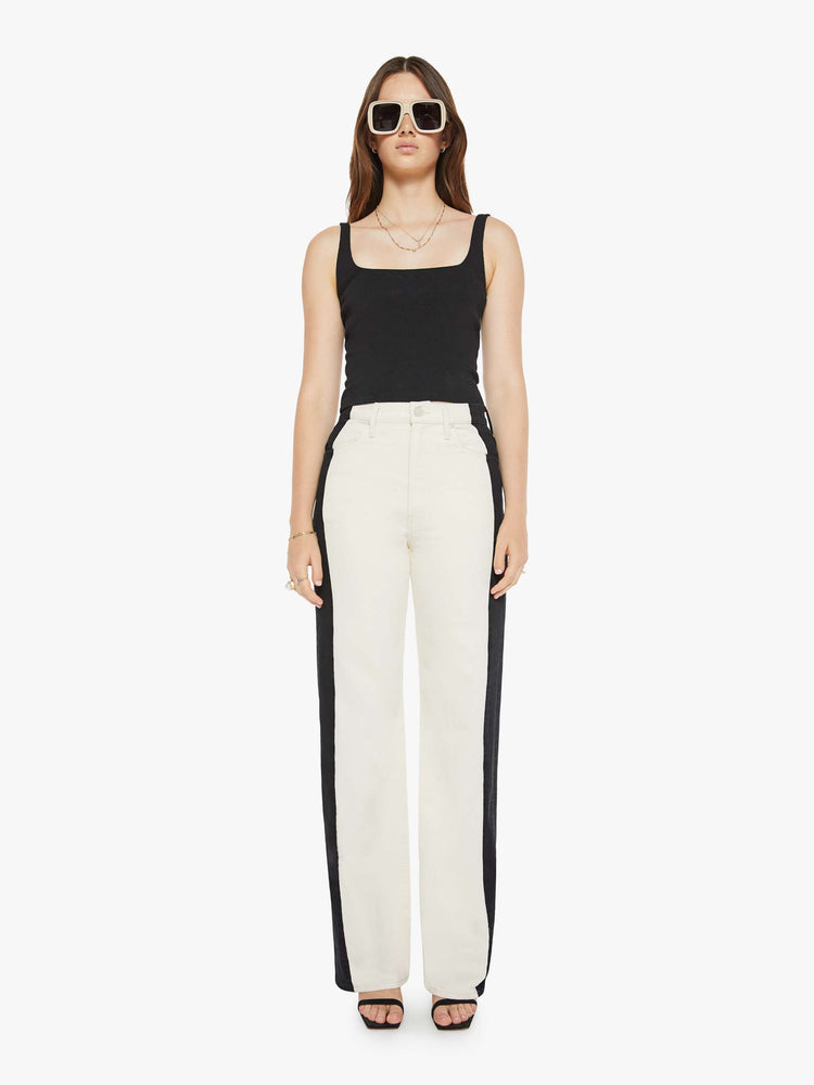 Front view of a woman super high-waisted pants with a loose fit, wide leg and a long 34-inch inseam with a clean hem in a cream color and a black stripe down the outer seam.