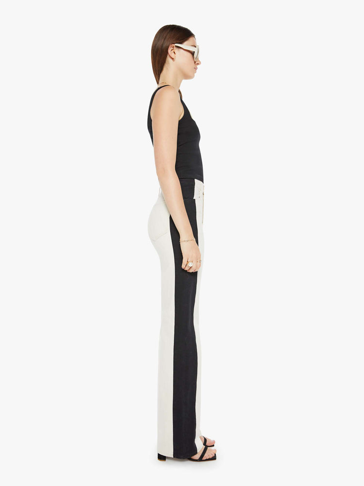 Side view of a woman super high-waisted pants with a loose fit, wide leg and a long 34-inch inseam with a clean hem in a cream color and a black stripe down the outer seam.