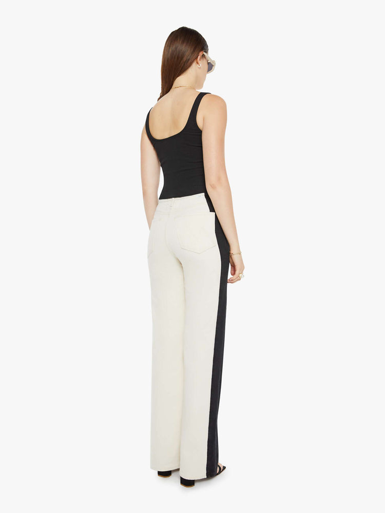 Back view of a woman super high-waisted pants with a loose fit, wide leg and a long 34-inch inseam with a clean hem in a cream color and a black stripe down the outer seam.