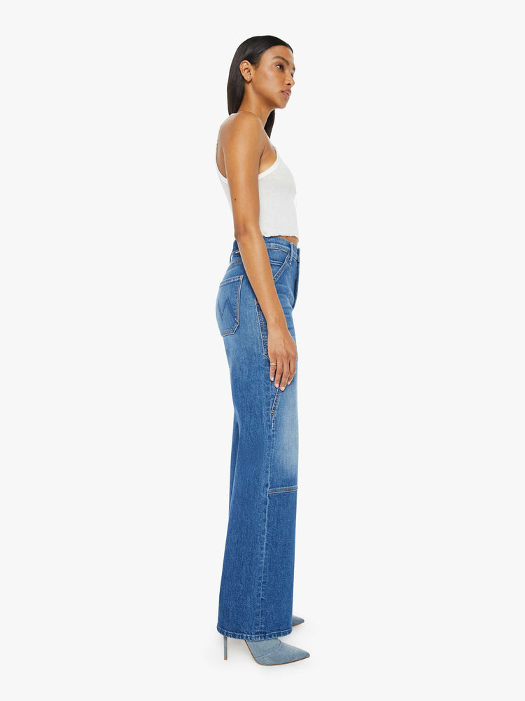 Side view of a woman in a mid blue wash wide-leg jeans with a super high rise, oversized front patch pockets, seamed details throughout and a long 32-inch inseam with a clean hem.