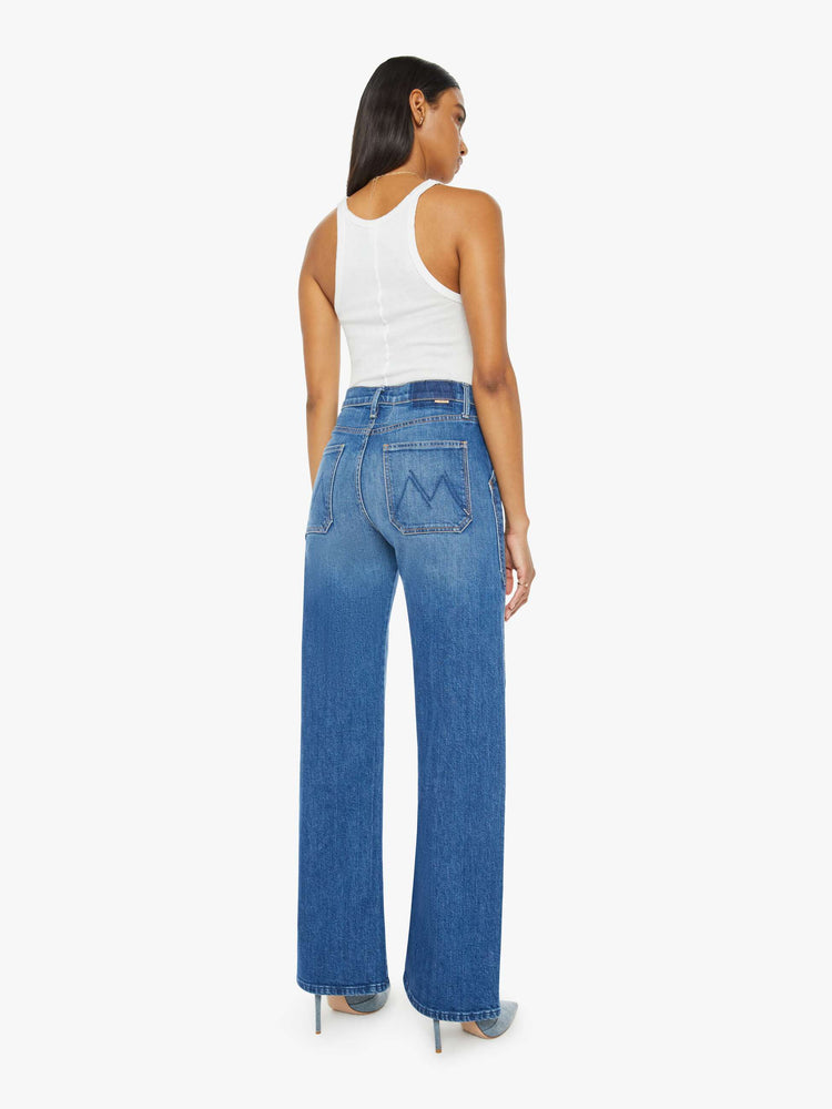 Back view of a woman in a mid blue wash wide-leg jeans with a super high rise, oversized front patch pockets, seamed details throughout and a long 32-inch inseam with a clean hem.