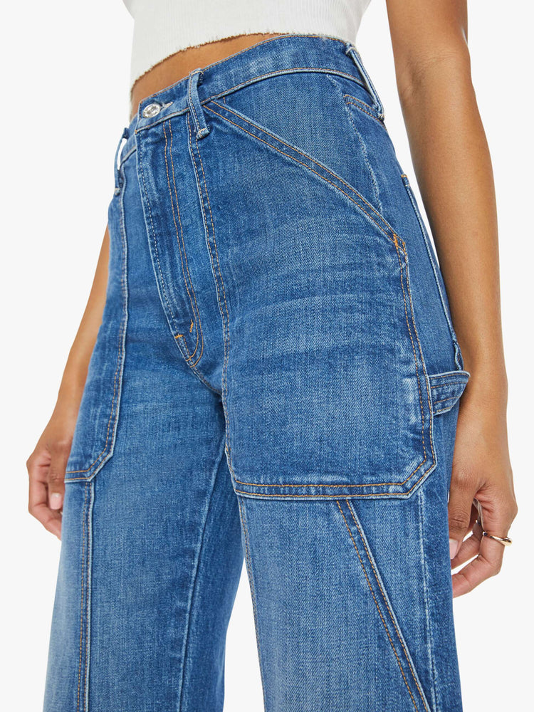 Waist close up view of a woman in a mid blue wash wide-leg jeans with a super high rise, oversized front patch pockets, seamed details throughout and a long 32-inch inseam with a clean hem.