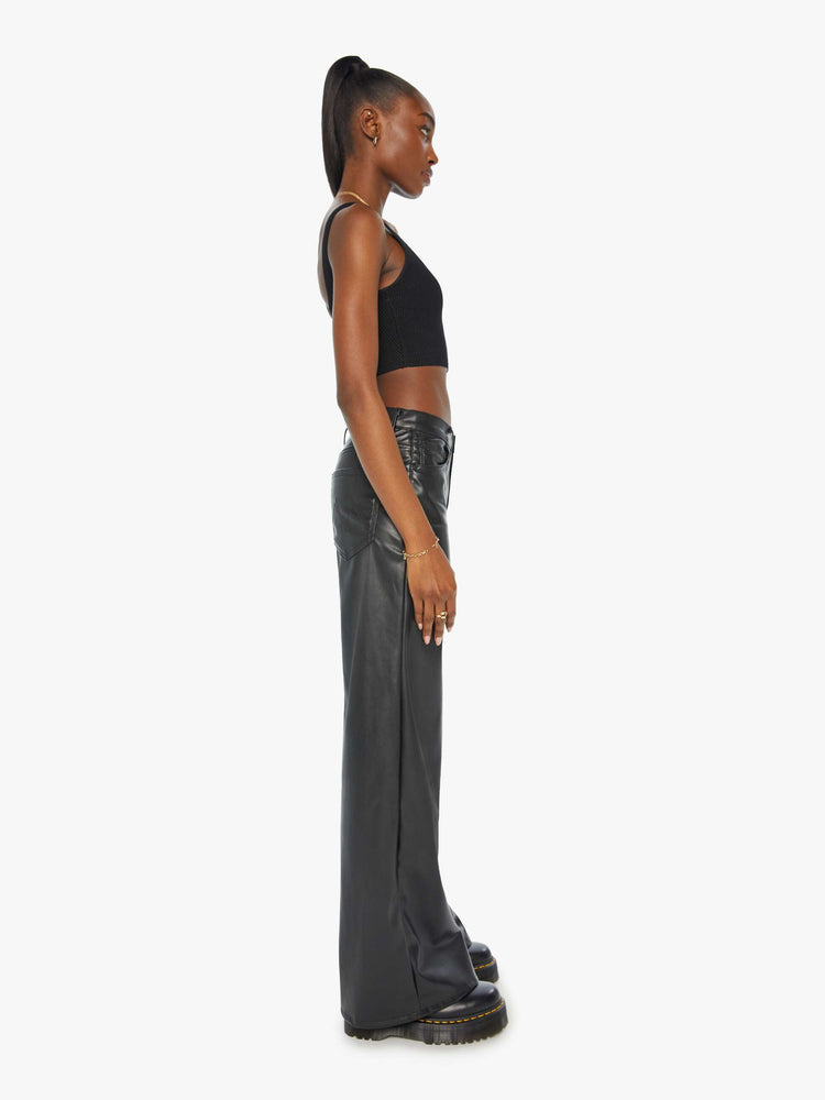 Side view of a woman black faux leather wide leg pants with a high rise, long 32-inch inseam and a clean hem.