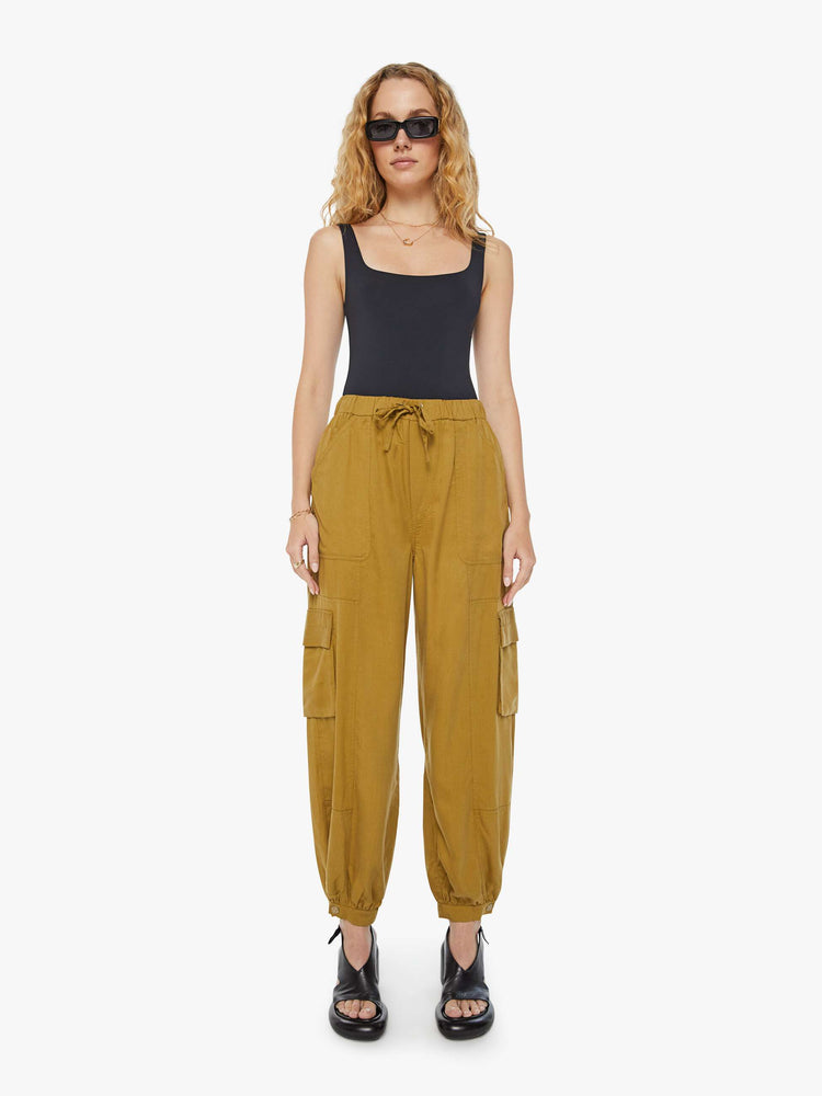 Front view of a woman in a bronze yellow high waisted cargo pant with an elastic drawstring waist, barrel leg, patch pockets and a long inseam with snaps at the hem. 