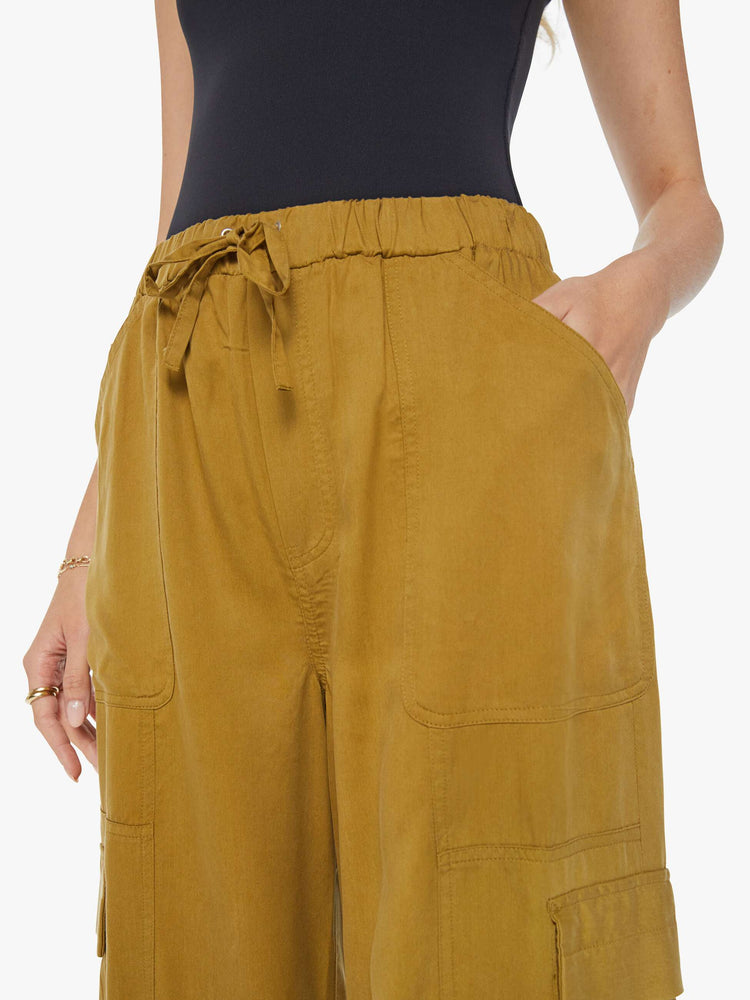 Swatch view of a woman in a bronze yellow high waisted cargo pant with an elastic drawstring waist, barrel leg, patch pockets and a long inseam with snaps at the hem.