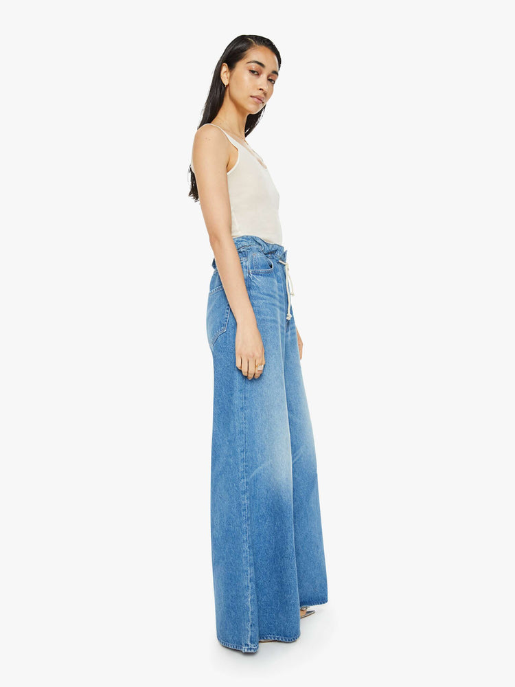 Side view of a woman in a light blue wash super high-rise jeans have a paper bag waist with a drawstring, an extra-wide, loose leg and a long 34-inch inseam with a clean hem.