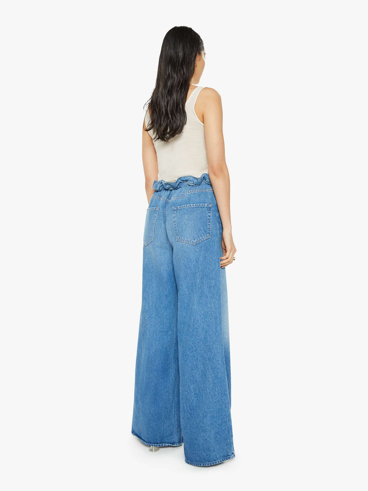 Back view of a woman in a light blue wash super high-rise jeans have a paper bag waist with a drawstring, an extra-wide, loose leg and a long 34-inch inseam with a clean hem.