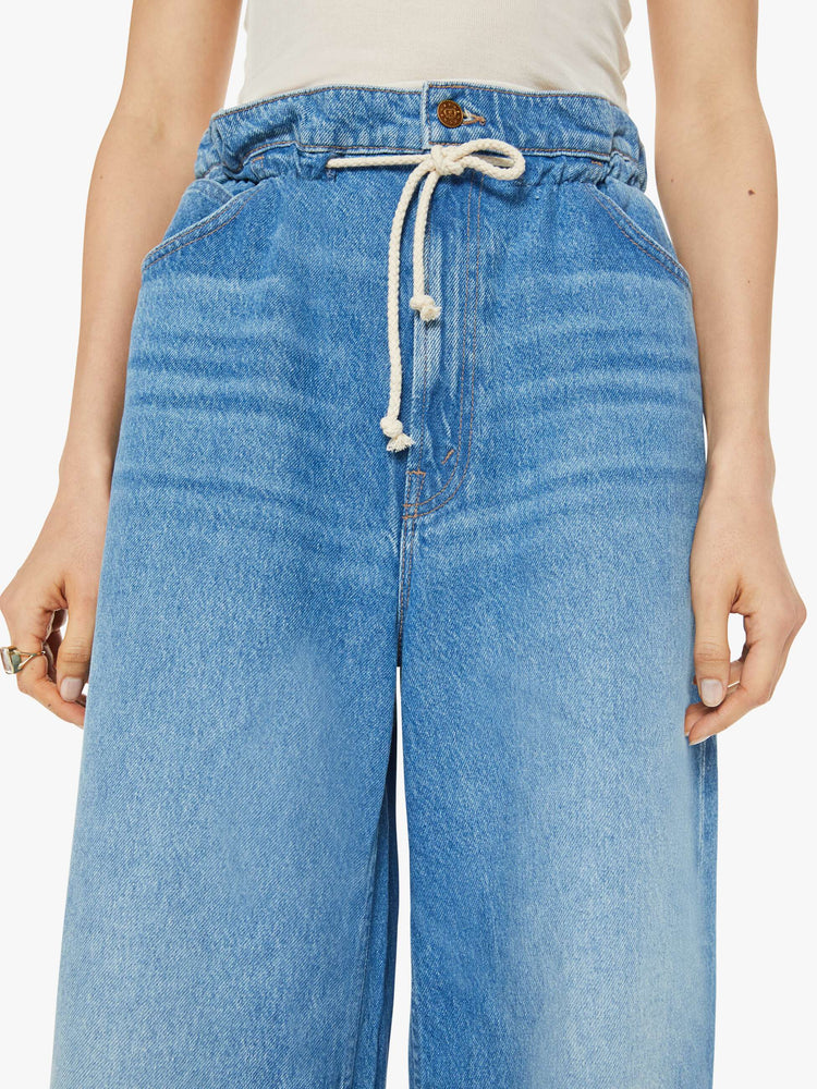 Waist close up view of a woman in a light blue wash super high-rise jeans have a paper bag waist with a drawstring, an extra-wide, loose leg and a long 34-inch inseam with a clean hem.