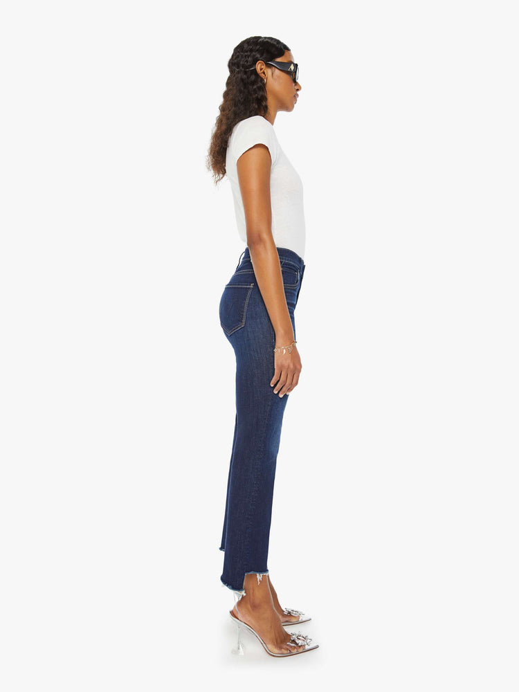 Side view of a woman in a dark blue high-waisted bootcut is cropped at the ankle with a frayed step-hem.