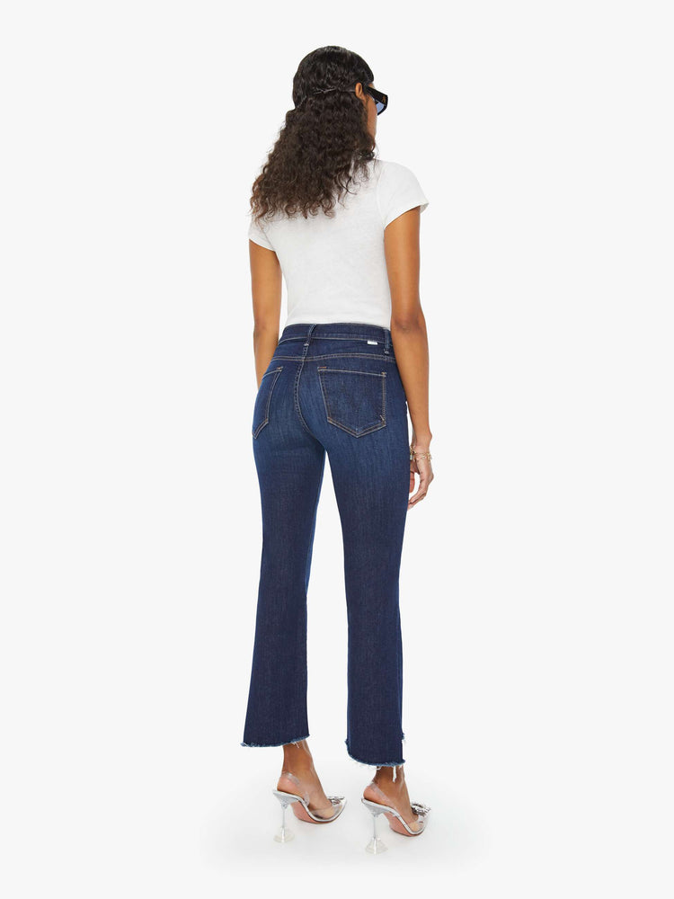 Back view of a woman in a dark blue high-waisted bootcut is cropped at the ankle with a frayed step-hem.