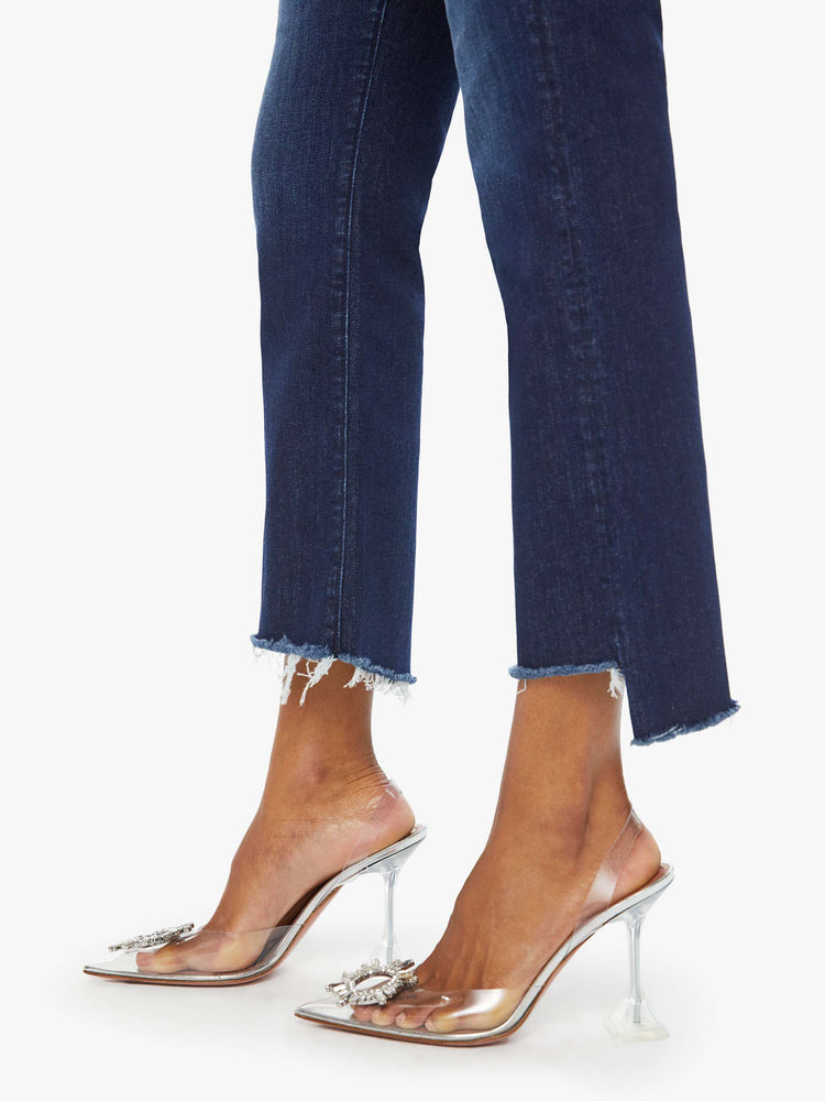 Hem view of a woman in a dark blue high-waisted bootcut is cropped at the ankle with a frayed step-hem.