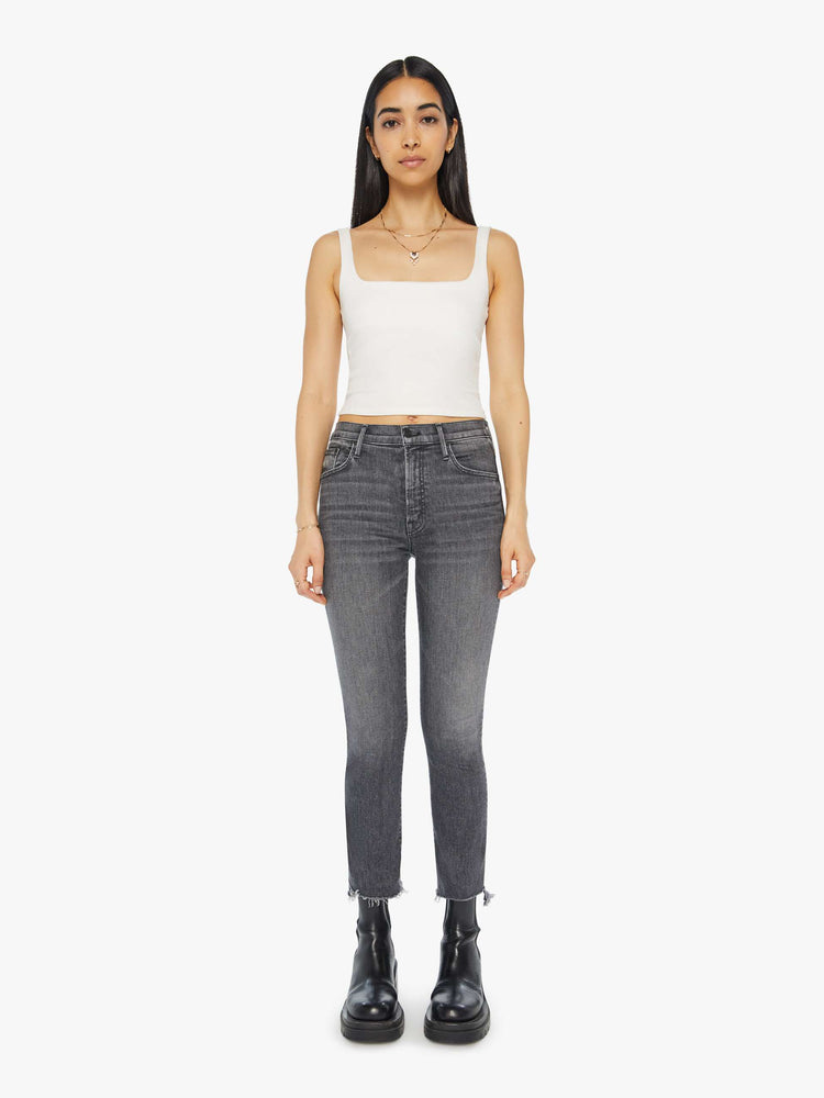 Front view of a woman in a high waisted bootcut that hits at the ankle with a frayed step hem in a dark grey wash.