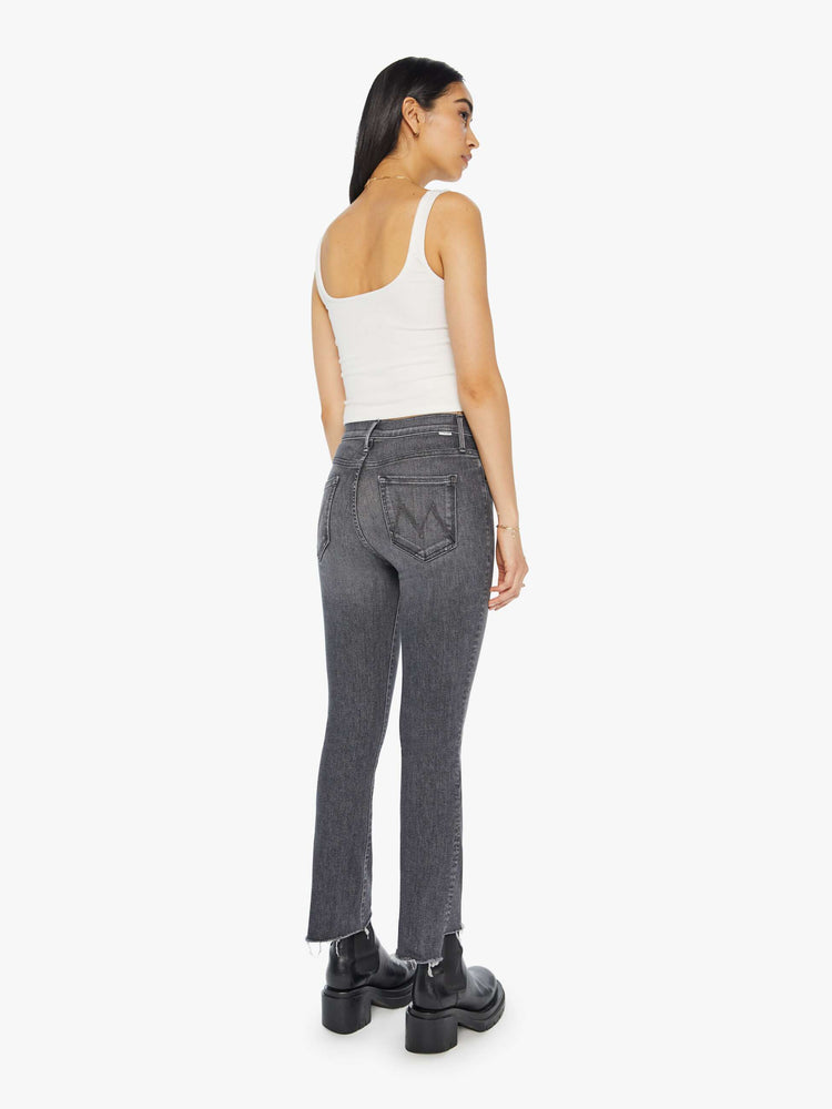 Back view of a woman in a high waisted bootcut that hits at the ankle with a frayed step hem in a dark grey wash.