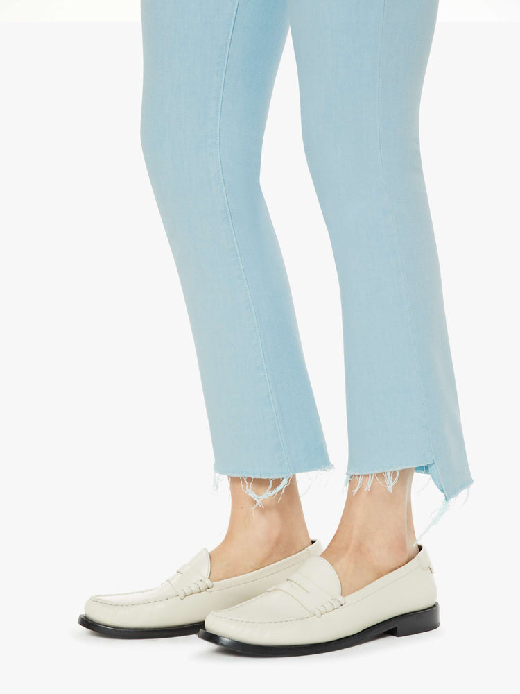 Hem view of a woman in high-waisted bootcut hits at the ankle with a frayed step hem in a bright sky blue.