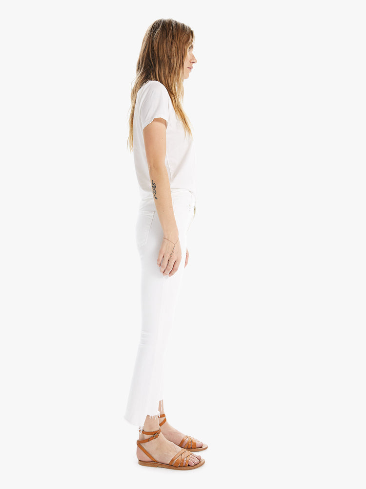 Side view of a women wearing a pair of white jeans with a step crop ankle.