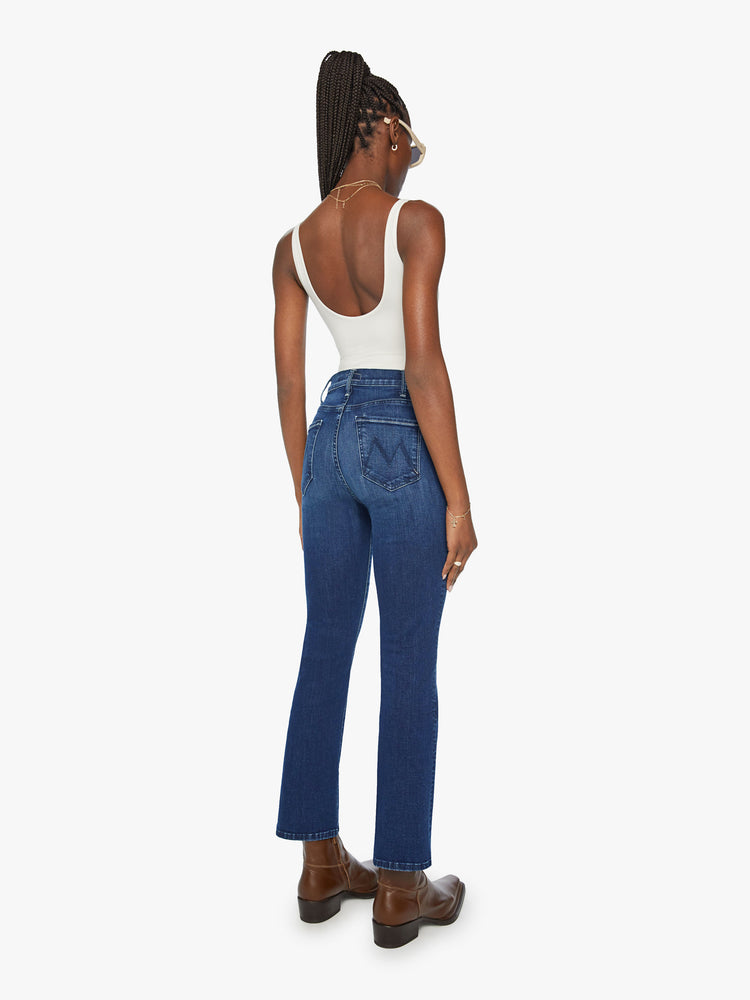 Back angle view of a woman in high-rise flare has an ankle-length inseam and a clean hem in a dark blue wash.