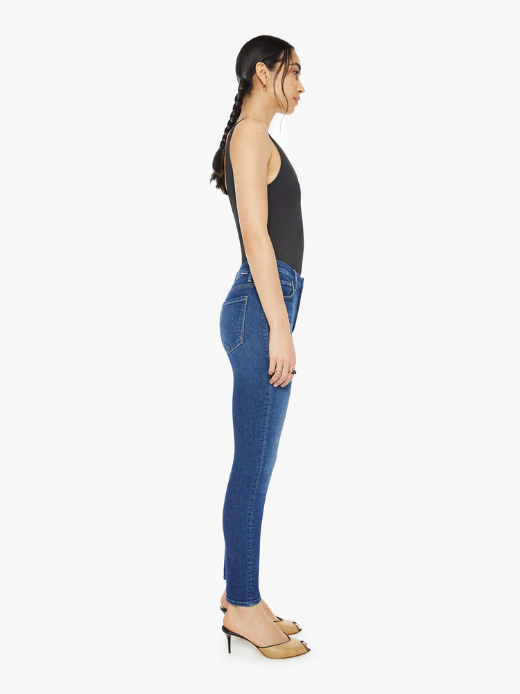 Side view of a woman in a dark blue skinny high rise with an ankle-length inseam and a clean hem.