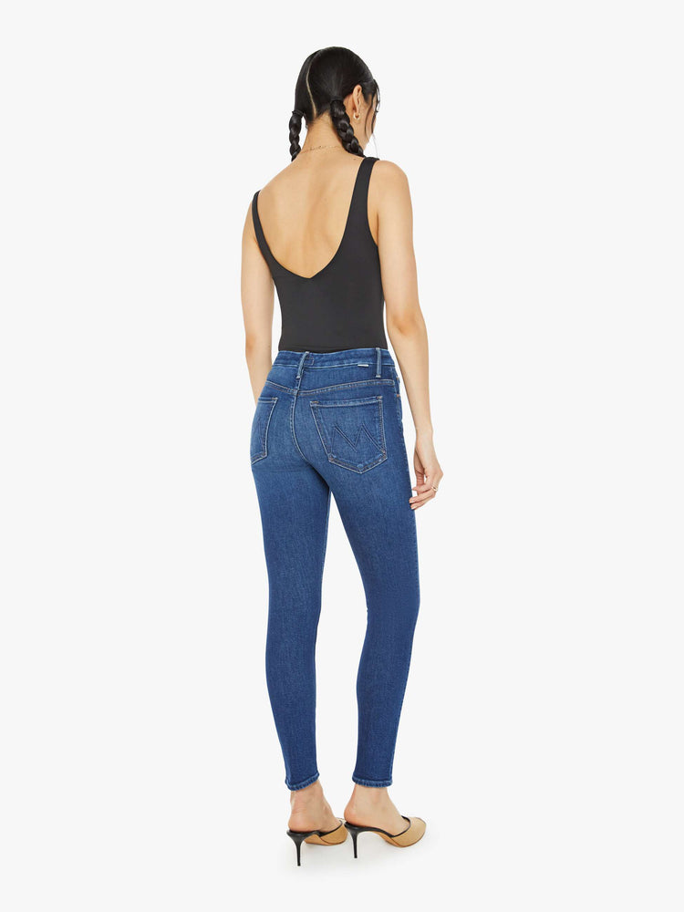 Back view of a woman in a dark blue skinny high rise with an ankle-length inseam and a clean hem.