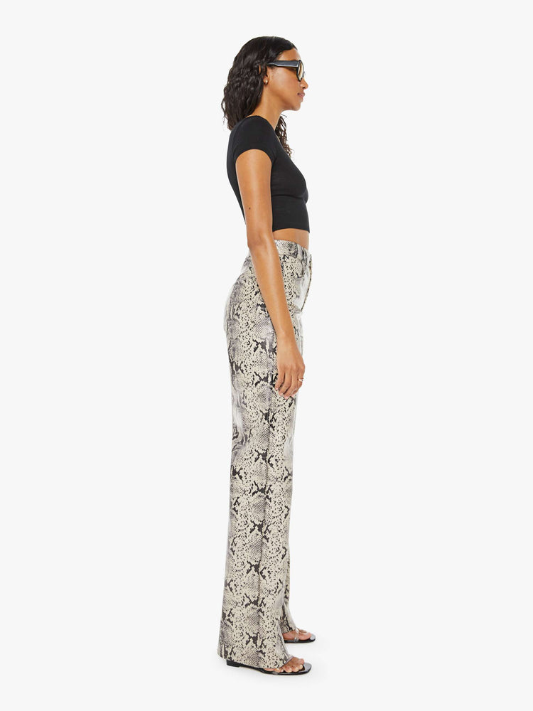 Side view of a woman super high-waisted pants with a loose fit, wide leg and a long 34-inch inseam with a clean hem in a cream and black snake print.