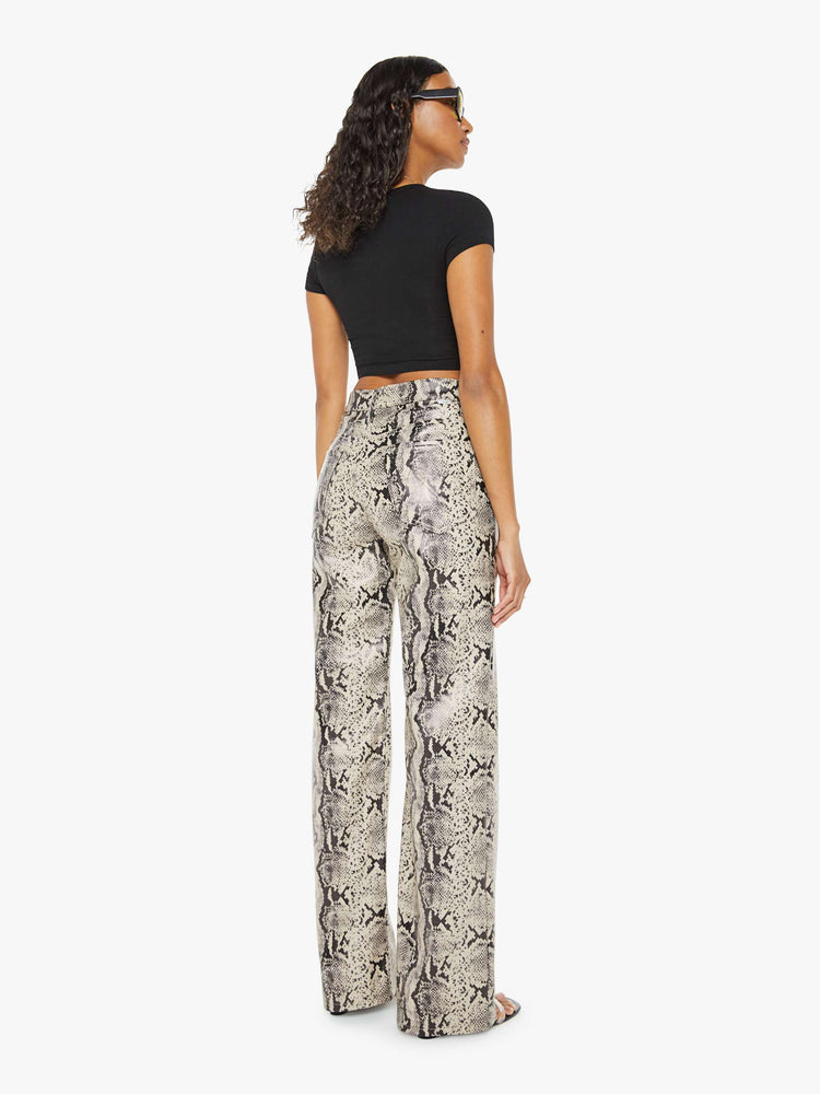 Back view of a woman super high-waisted pants with a loose fit, wide leg and a long 34-inch inseam with a clean hem in a cream and black snake print.