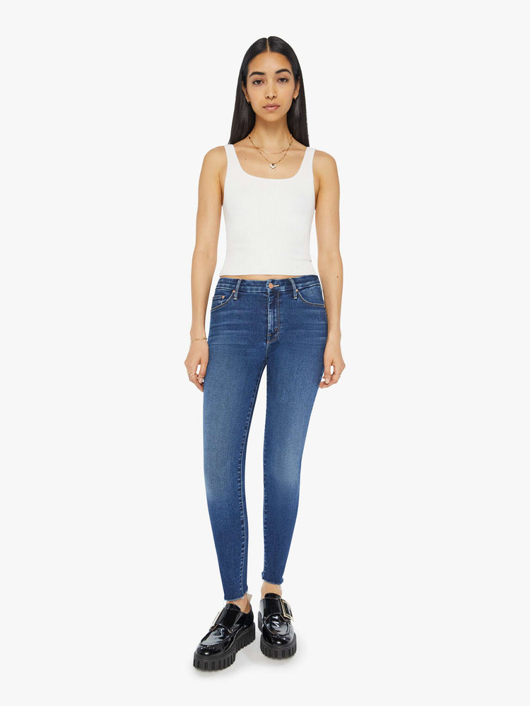 Front view of a woman in a dark blue mid-rise skinny jean with an ankle-length inseam and a frayed hem.