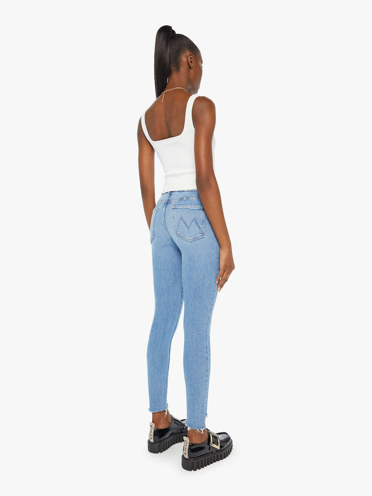 Back view of a woman in a light blue wash high-rise skinny jean has an ankle-length inseam and a frayed step hem.