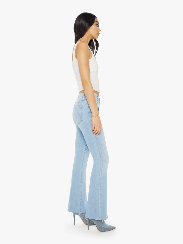 Side view of a woman in a mid-rise flare has a 31-inch inseam with a frayed hem in a light blue wash.