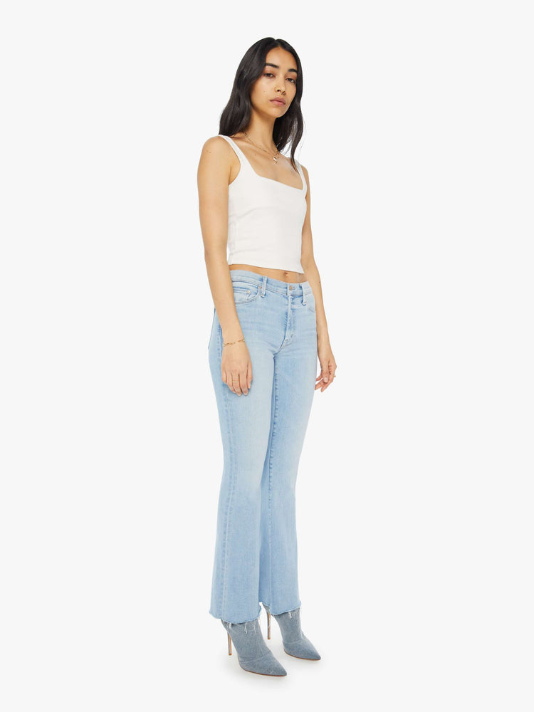 Side angle view of a woman in a mid-rise flare has a 31-inch inseam with a frayed hem in a light blue wash.