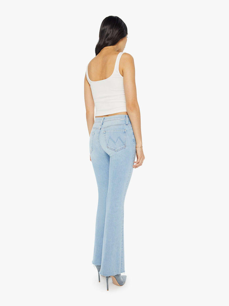 Back view of a woman in a mid-rise flare has a 31-inch inseam with a frayed hem in a light blue wash.