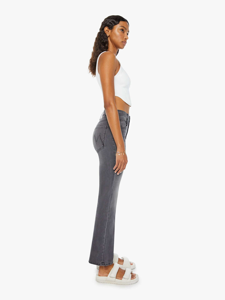 Side view of a woman in high-rise flare with a button fly and a clean ankle-length hem dark grey wash.