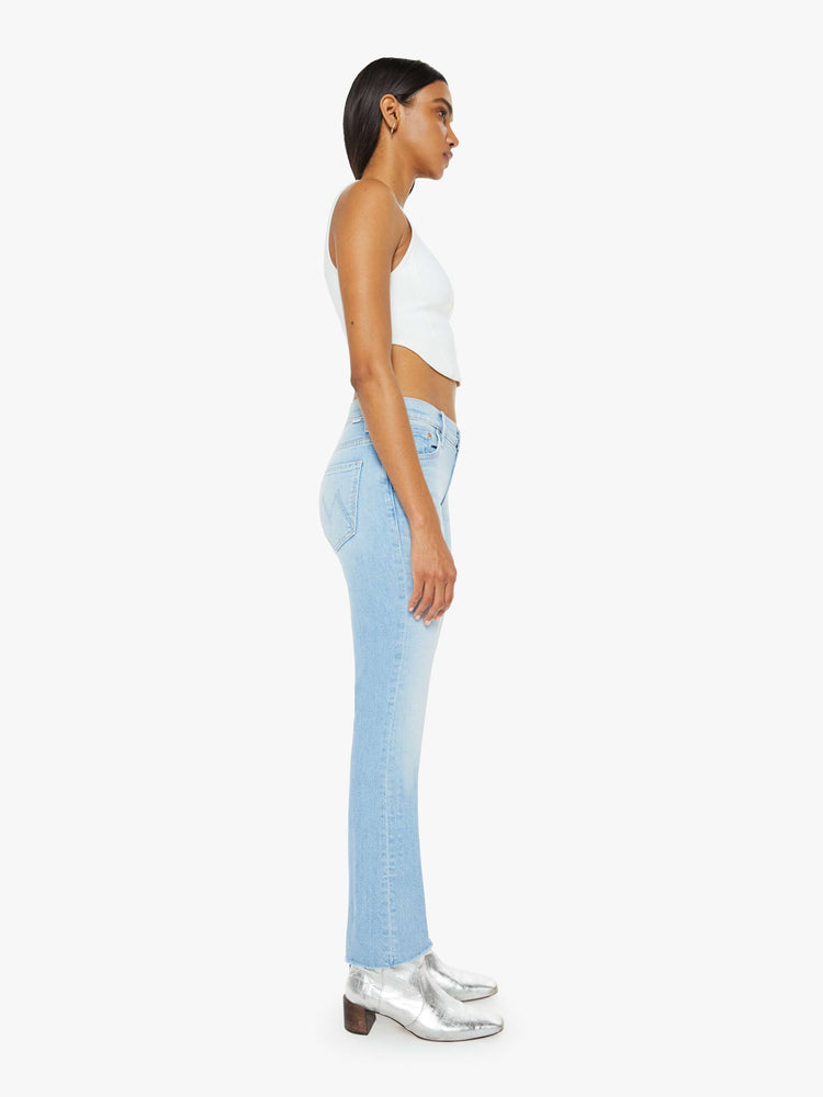 Side view of a woman in a light blue wash high-rise bootcut has an ankle-length inseam and a frayed hem. 