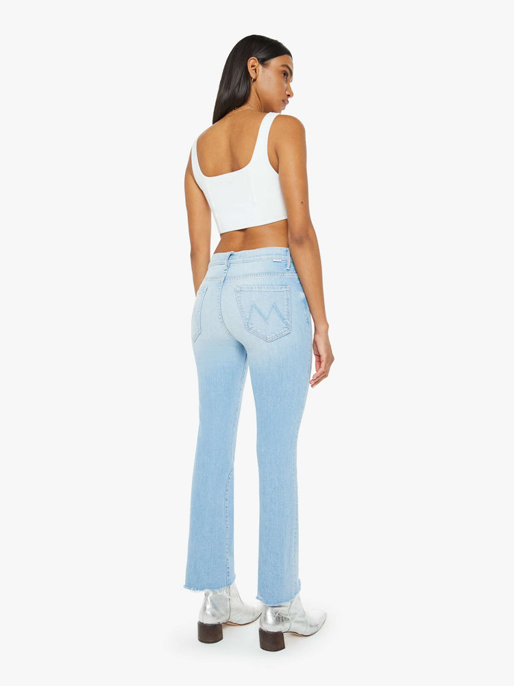 Back view of a woman in a light blue wash high-rise bootcut has an ankle-length inseam and a frayed hem. 