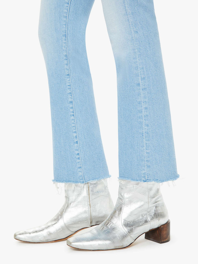 Hem view of a woman in a light blue wash high-rise bootcut has an ankle-length inseam and a frayed hem. 