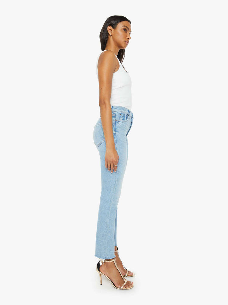 Side view of a woman in light blue  high-rise straight leg has an exposed button fly and a frayed ankle-length inseam. 