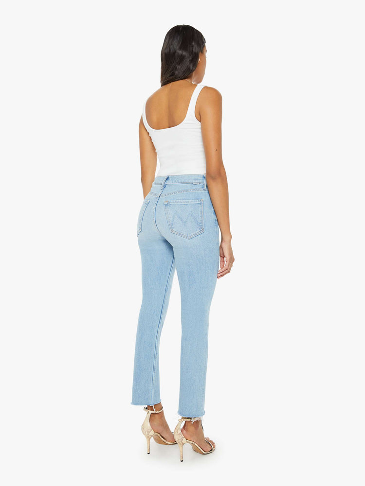 Back view of a woman in light blue  high-rise straight leg has an exposed button fly and a frayed ankle-length inseam. 