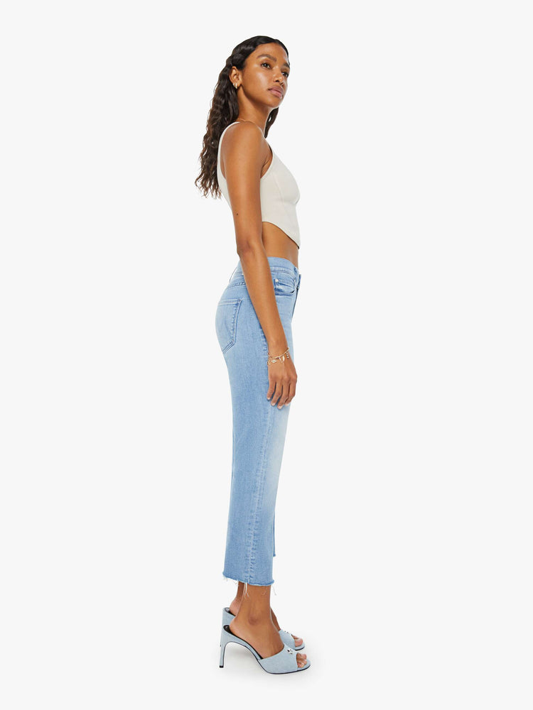 Side view of a womens light blue wash denim jean featuring a mid rise and a frayed crop hem.