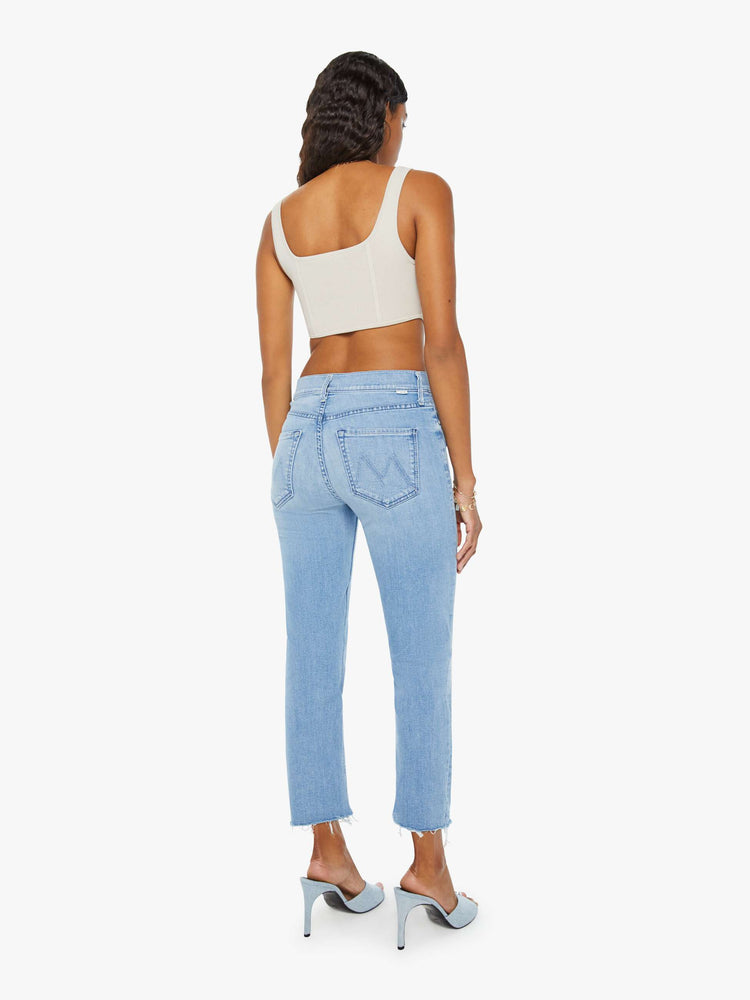 Back view of a womens light blue wash denim jean featuring a mid rise and a frayed crop hem.