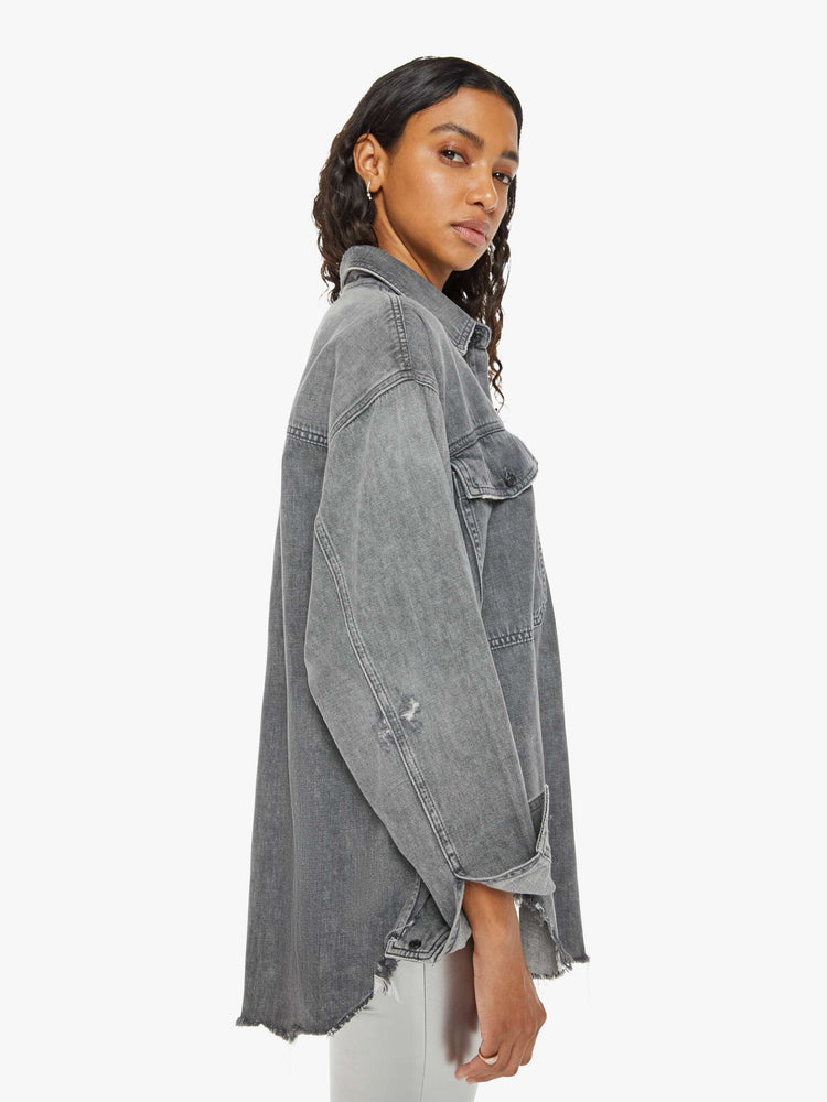 Side view of a woman  oversized button-up with drop shoulders, extra-large patch pockets and a frayed, curved hem in a dark grey.