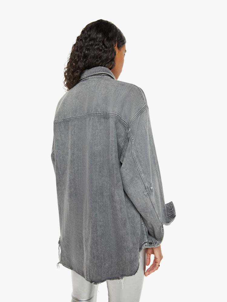 Back view of a woman  oversized button-up with drop shoulders, extra-large patch pockets and a frayed, curved hem in a dark grey.