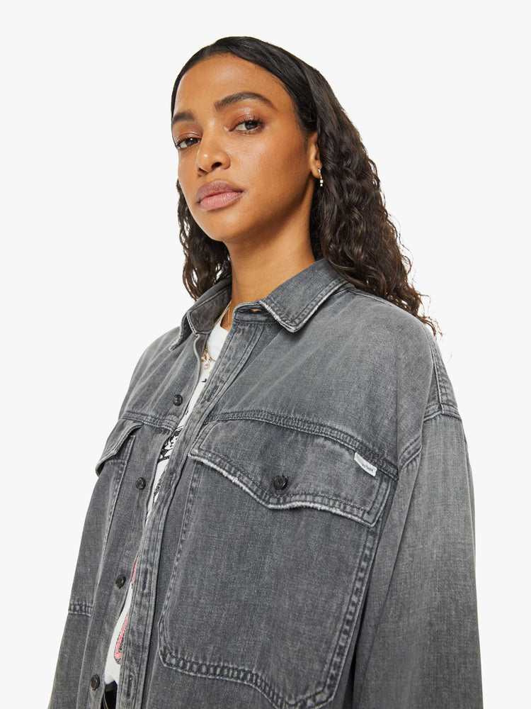 Close up view of a woman  oversized button-up with drop shoulders, extra-large patch pockets and a frayed, curved hem in a dark grey.