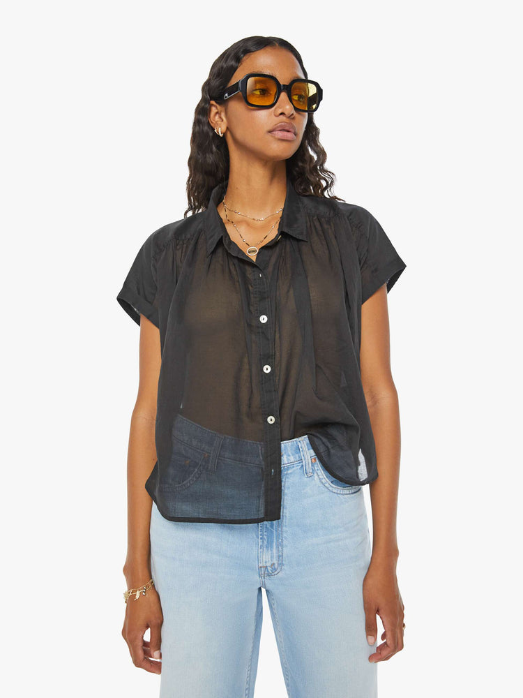 Front view of a woman in a sheer dark grey button-up blouse with short sleeves and ruffles around the collar for a loose, flowy fit.