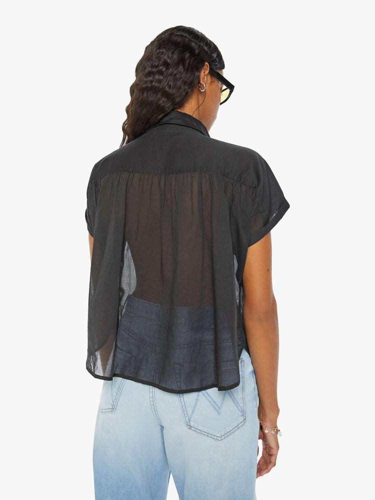 Back view of a woman in a sheer dark grey button-up blouse with short sleeves and ruffles around the collar for a loose, flowy fit.