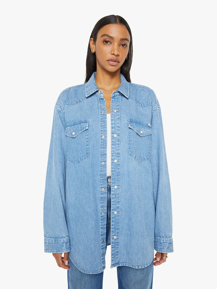 Front view of a woman in vintage blue wash  denim button-up with drop shoulders, front patch pockets, a Western-inspired yoke and a curved hem. 