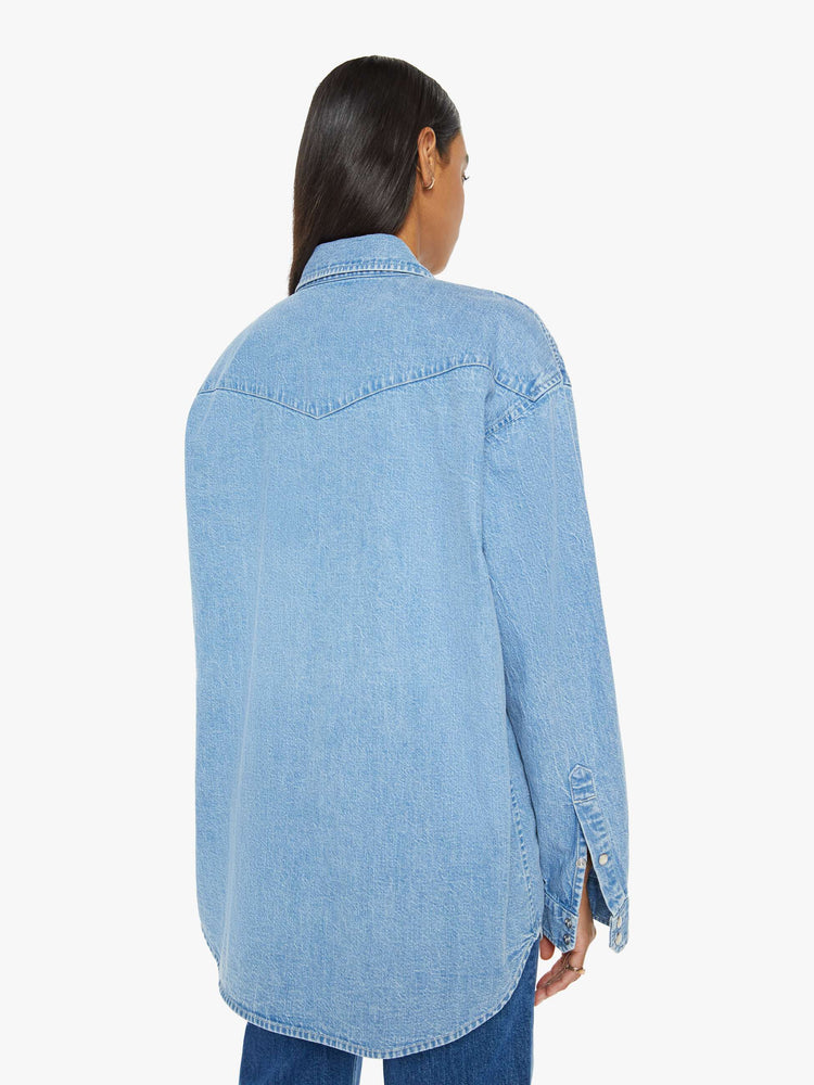 Back view of a woman in vintage blue wash  denim button-up with drop shoulders, front patch pockets, a Western-inspired yoke and a curved hem. 