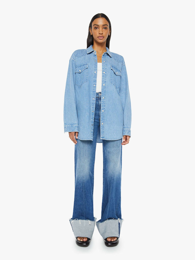 Full body view of a woman in vintage blue wash  denim button-up with drop shoulders, front patch pockets, a Western-inspired yoke and a curved hem. 