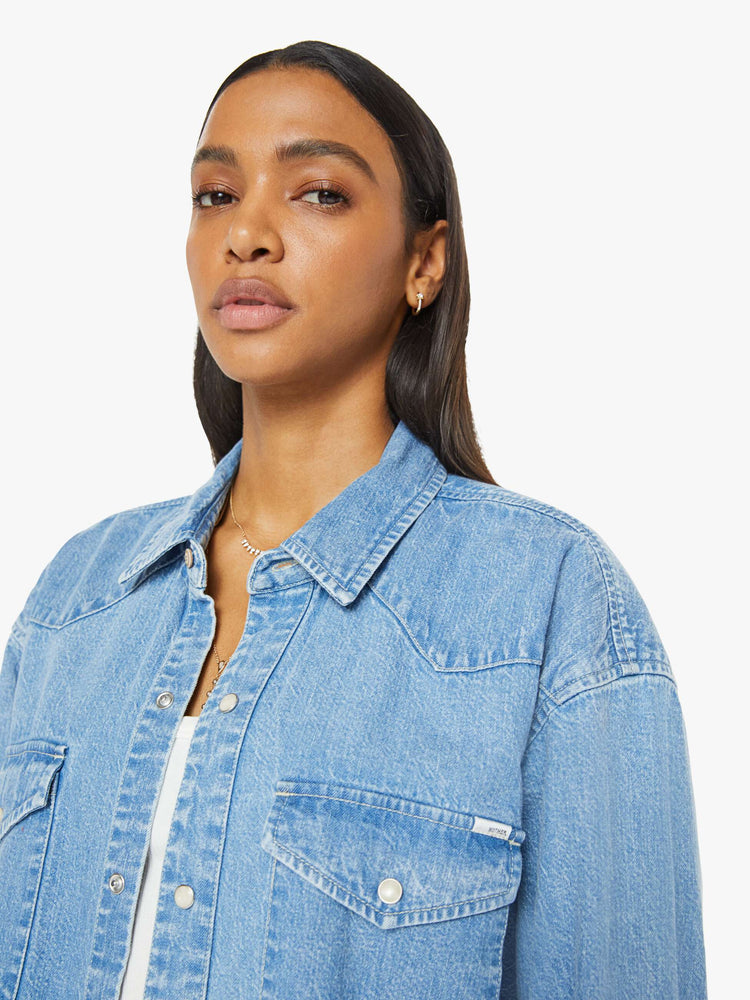 Close up view of a woman in vintage blue wash  denim button-up with drop shoulders, front patch pockets, a Western-inspired yoke and a curved hem. 