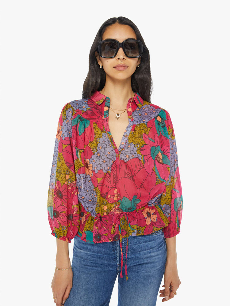 Front view of a woman in a collared V-neck blouse with 3/4-length balloon sleeves, a tied waist and ruffles throughout for a loose, flowy fit in a floral print.