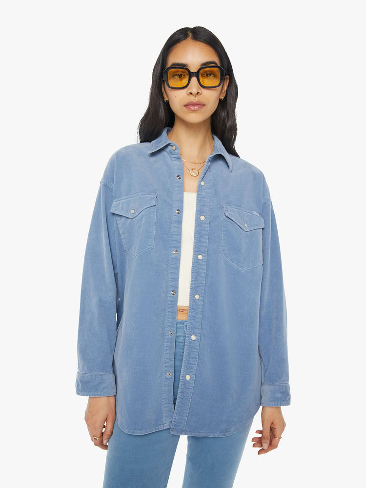 Front view of a woman light blue corduroy western-inspired button-up with drop shoulders, patch pockets, snap closures and a curved hem.