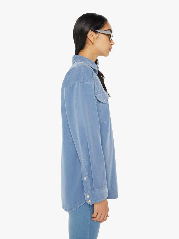 Side view of a woman light blue corduroy western-inspired button-up with drop shoulders, patch pockets, snap closures and a curved hem.