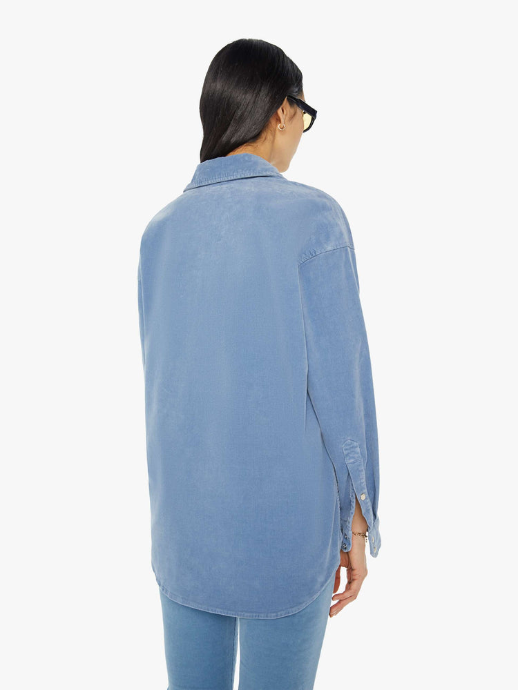 Back view of a woman light blue corduroy western-inspired button-up with drop shoulders, patch pockets, snap closures and a curved hem.